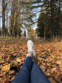 a person's feet resting on leaves in the middle of a wooded area with trees