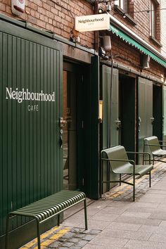 two green benches sitting next to each other in front of a brick building on a city street