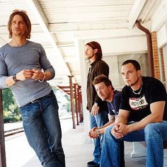 four men are sitting on benches and one man is holding a cell phone in his hand