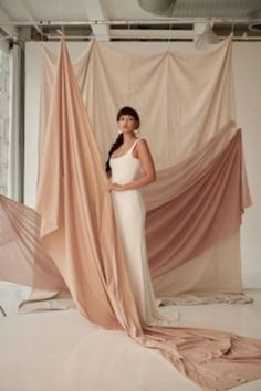 a woman in a white dress standing next to some pink draping on the floor