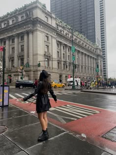 a woman walking across a street in front of a tall building with lots of windows