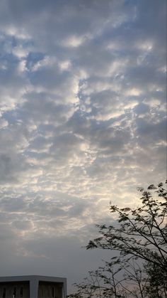 an airplane is flying high in the sky above some trees and buildings on a cloudy day