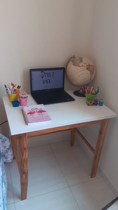 a laptop computer sitting on top of a white desk next to a cup filled with pencils