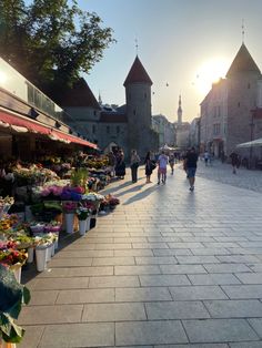 people are walking down the street in front of some flowers and plants on display at an outdoor market