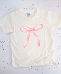 Our Pink Bow graphic tee is made with 100% polyester, ensuring durability and a comfortable fit. The cowboy design adds a fun and unique touch, making it perfect for any young adventurer. Upgrade their wardrobe with this high-quality tee today! *Don’t forget to choose your color tee: CREAM or WHITE *All tee brands run true to size. The graphic used on our tees are sublimation prints which means its printed into the fabrics on the shirt. No more peeling! *Care Instructions: Turn inside out & wash Cute Simple Shirt Designs, Cute Shirts Aesthetic Trendy, Making Graphic Tees, Bow T-shirt, Bow Tshirts, Pink Shirt Aesthetic, Pink Shirt Design, Mini Tees, Simple Shirt Design