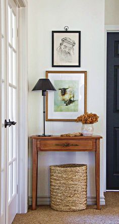 an entryway with a table, lamp and pictures hanging on the wall above it