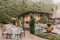 an outdoor dining area with tables, chairs and a fountain in the center surrounded by greenery