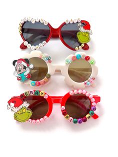 "CHRISTMAS SUNNIES!! These are so adorable-- and make the perfect stocking stuffers!! Each pair is handcrafted by me. Using various beads, Charms, Rhinestones, and fun details! ♥️ *3 options available-- Choose your style:  1. MERRY MINI 2. RESTING GRINCH FACE 3. MERRY GRINCHMAS * Anti-Glare * UV Protection (UVA & UVB) * Durable and shatterproof  * They open and close smoothly  * Each item is made to order and will be ready to ship in 5-7 business days! If you need your order sooner. Please check out my \"RUSH ORDER OPTION\".  https://www.etsy.com/EyeCandyandFluff/listing/1286351273/rush-my-order-please *SHOP DISCLAIMER/WAIVER!  * Do NOT let your child put the sunglasses in their mouth as beads can become detached.    Always monitor and supervise while children are wearing these. The shop a Playful Red Sunglasses For Party, Fun Handmade Sunglasses As A Gift, Cute Customizable Sunglasses For Gift, White Plastic Sunglasses For Gift, Playful White Sunglasses For Gift, White Plastic Sunglasses As Gift, Playful White Sunglasses As Gift, Playful White Sunglasses For Gifts, Cute Red Sunglasses With Uv Protection