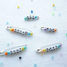 three different colored beads with the word squad hanging from them on a white surface surrounded by confetti