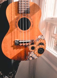 a ukulele with sunflowers on it sitting in front of a window