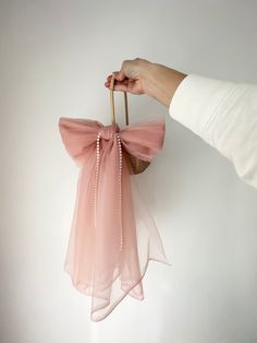 a hand holding a pink bag with a bow hanging from it's side on a white wall