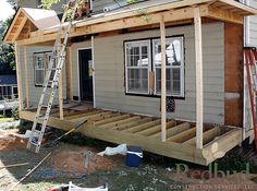 a house being built with wooden boards and ladders on the front porch, next to a tree