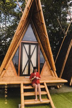 a woman sitting on top of a wooden structure in the grass next to some trees