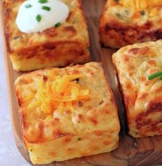 several square pieces of food on a wooden tray with cheese and sour cream toppings