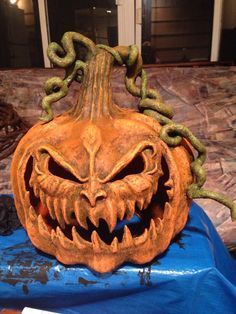 a carved pumpkin with an evil face on it's head is sitting on a blue tarp