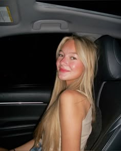 a woman sitting in the back seat of a car smiling at the camera with long blonde hair