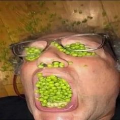 a man with green peas on his face and glasses covering his eyes as if he was eating something