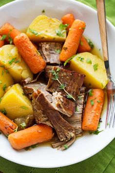 a white bowl filled with meat, potatoes and carrots on top of a green table cloth