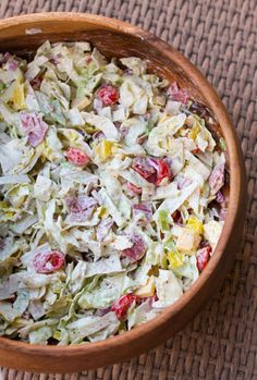 a wooden bowl filled with salad sitting on top of a woven tablecloth covered floor