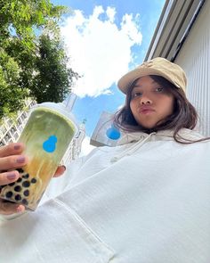 a woman holding a drink in her right hand and wearing a hat on top of her head