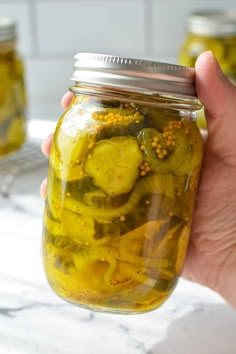 a person holding a jar filled with pickles on top of a white countertop