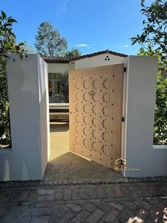 an open door to a house with a bench in the back ground and trees behind it