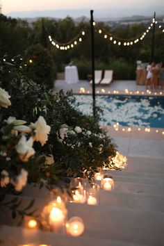 candles are lined up along the edge of a pool with flowers and lights around it