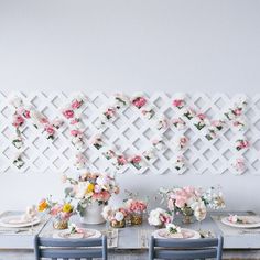 a dining room table set for four with flowers on the wall and plates in front of it