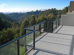 a balcony with glass railings overlooking trees and mountains