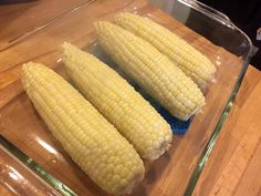 three corn on the cob are sitting in a glass dish, ready to be cooked