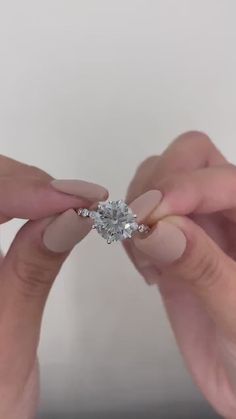 two hands holding an engagement ring in front of the camera with their fingers touching it