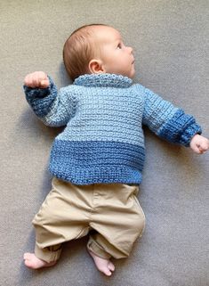 a baby laying on the floor wearing a blue sweater