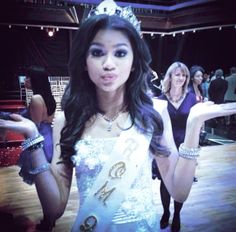 a beautiful young lady wearing a tiara standing in front of a group of women