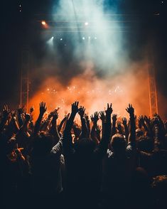 a crowd of people at a concert with their hands in the air and lights on