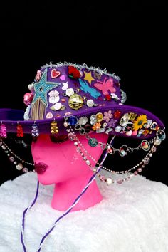 All eyes will be on you in this fabulous purple cowgirl hat covered to the brim with rainbow galore. From the front hang colorful gummy bears and from the sides hang three colorful beaded chains. The hat is covered with stars, hearts, flowers, rhinestones, butterflies, pearls, disco balls, mini animals and treats, and silver tinsel. It has a purple and lace neck tie. Playful Purple Adjustable Hat, Whimsical Adjustable Purple Costume Hats And Headpieces, Novelty Wide Brim Festival Costume Hat, Novelty Wide Brim Costume Hat For Festivals, Novelty Wide Brim Costume Hats And Headpieces For Festivals, Fun Adjustable Mini Hats For Rodeo, Handmade Purple Party Hat, Purple Hat For Spring Festival, Novelty Curved Brim Hat For Festival