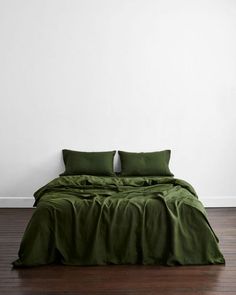 a bed with green sheets and pillows on top of it in front of a white wall