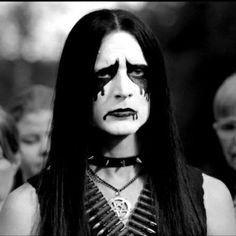 a woman with black makeup and white make - up is standing in front of other people