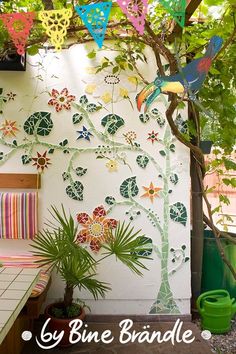 an outdoor area with a bench, potted plant and colorful paper flowers on the wall