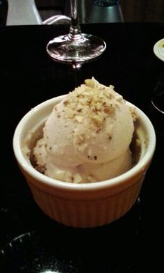 an ice cream sundae in a paper cup on a black table with two wine glasses