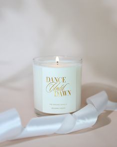 a white candle sitting on top of a table next to a piece of paper that says dance with the dawn