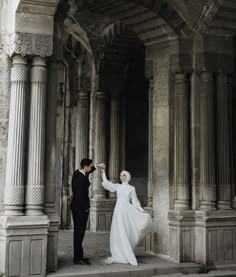 a man and woman standing in an old building with columns on either side of them