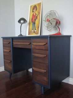 a wooden desk with two drawers and a fan on top of it in a room