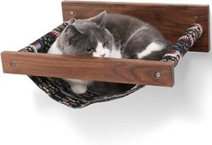 a gray and white cat laying in a hammock on top of a wooden shelf