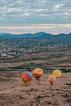 three hot air balloons in the desert with mountains in the background and clouds in the sky