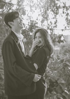 a man and woman standing next to each other in front of some trees with string lights