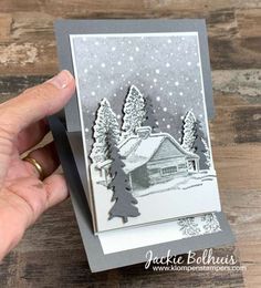 someone holding up a christmas card with a house in the snow and trees on it