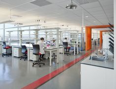 two men in white lab coats working at desks with red and black chairs on each side