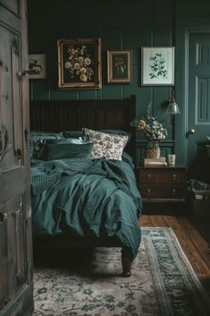 a bedroom with dark green walls and wooden bed frame, blue comforter, floral throw pillows, and rug