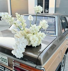 white flowers are placed in a vase on the hood of a brown station wagon car