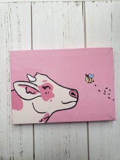 a painting of a cow with a bee on it's nose is hanging on a white wooden wall